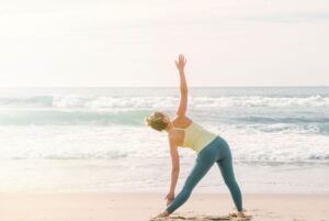 A woman performing yoga on a beach.